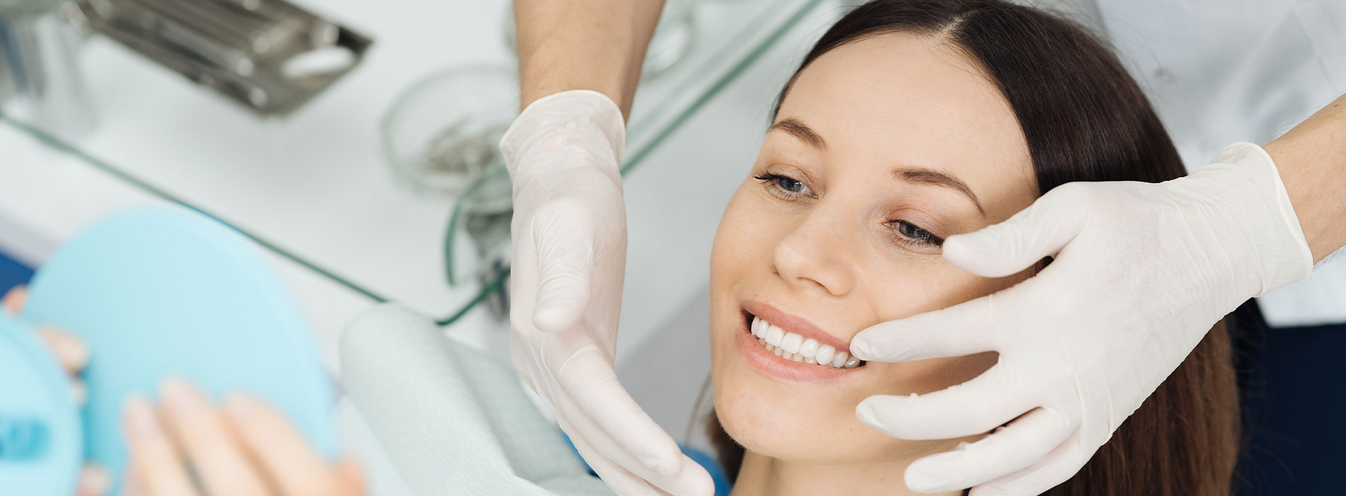 A woman receiving a facial treatment with a smiling expression, while a person in white gloves applies a product to her face.